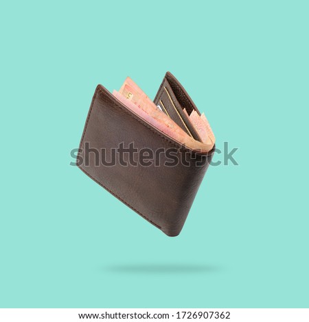 Flying in air Brown genuine leather wallet with banknotes and credit card inside isolated on turquoise background. Сток-фото © 