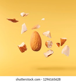 Flying in air fresh raw whole and cut almonds  isolated on yellow background. Concept of Almonds is torn to pieces close-up. High resolution image
