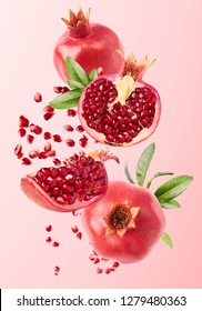 Flying in air fresh ripe whole and cut pomegranate with seeds and leaves isolated on pastel pink background. High resolution image