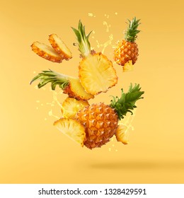 Flying in air fresh ripe whole and cut baby Pineapple with juice splash isolated on pastel yellow background. High resolution image
