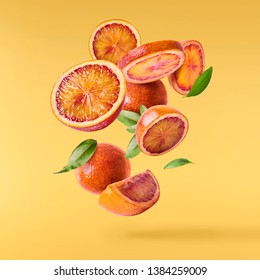 Flying in air fresh ripe whole and cut blood orange with leaves isolated on pastel yellow background. High resolution image