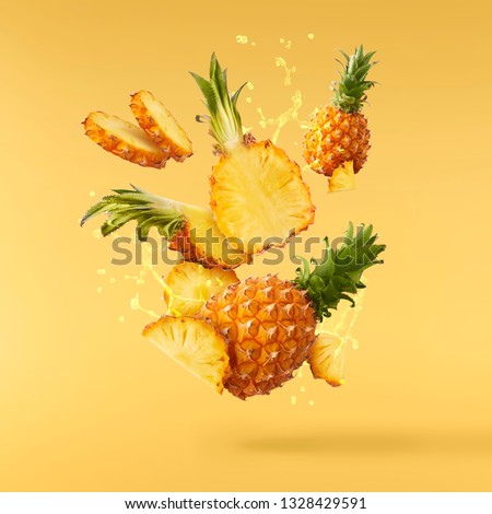 Flying in air fresh ripe whole and cut baby Pineapple with juice splash isolated on pastel yellow background. High resolution image