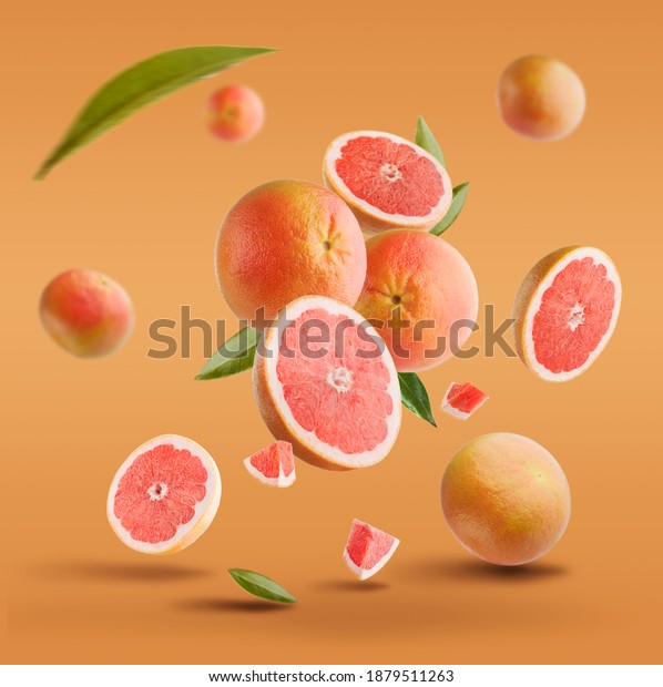 Flying in air fresh ripe\
whole and cut grapefruit with seeds and leaves isolated on red\
background.