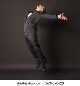 Flying In The Air A Man On A Black Background In A Tuxedo With Wide Open Hands, Lacquered Shoes, Jumping