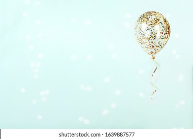 Flying balloon with shiny gold confetti and ribbon on light blue background. Sparkles wallpaper decor. Happy birthday, valentine, wedding invitation greeting cart.