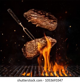 Flying beef steaks over flaming grill grid, isolated on black background. Barbecue and cooking