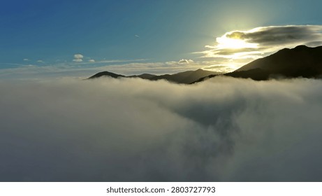 Flying between the clouds. Aerial view of clouds, sun, and mountains at sunrise. Traveling by air background