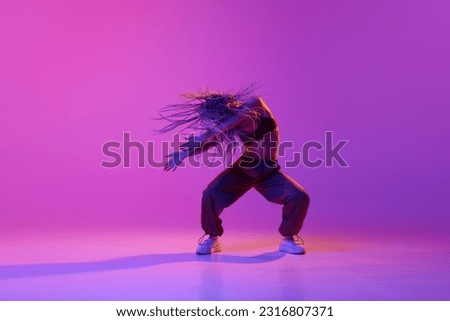 Flying braided dreads. Portrait with one young girl, inspired dancer with pigtails dancing with hands over gradient purple background in neon light. Contemporary dance style, motion, art, ad concept