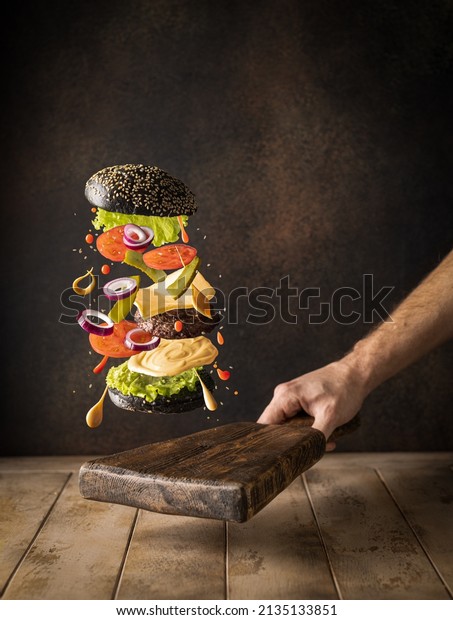 Flying burger\
ingredients: bun, salad, leaves, sauce, tomatoes, cucumber, meat\
and red onion on wooden background with copy space. Food\
levitation. Burger in freeze\
motion.