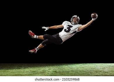 Flying, Catching Ball. Portrait Of American Football Player Training Isolated On Dark Studio Background With Green Grass Flooring. Concept Of Sport, Movement, Achievements. Copy Space For Ad