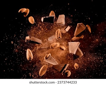 Flying chocolate peaces and almonds in cocoa powder explosion on black background