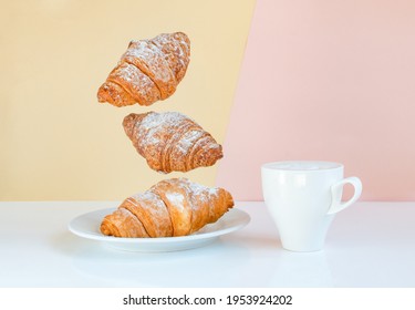 Flying croissants for breakfast and a cup of coffee on a beige background color sunrise. Levitating food, time to wake up call. Modern breakfast still life concept food.