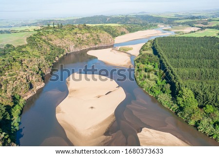 Flying down large wide river overhead with low water sandbanks through rural farmlands