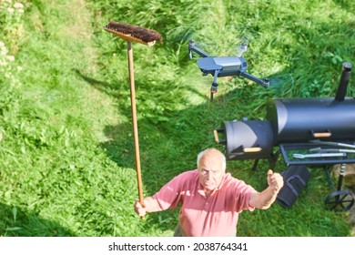 Flying drone over the garden and an angry old man trying to drop a drone with a broom from the sky. Privacy violation concept. Selective focus. Breaking the rules when flying drone. Illegal flying 