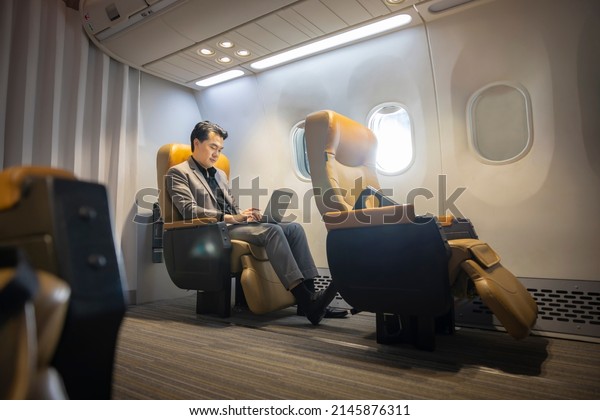 Flying at first class. Asian businessman working on\
laptop using wireless connection on board and thinking, analyzing\
data while sitting comfortable seat in airplane cabin business\
class. Copy space  