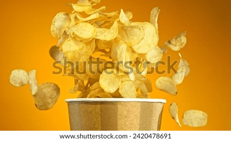 Flying Fried Potato Chips Exploding from Paper Bucket. Concept of Flying Junk Food.