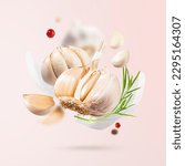 Flying Garlic falling in air with red and black pepper and herbs like dill and fennel leaves on light pink background. Spicy and fragrant seasoning food for cooking.Creative food concept. Modern photo