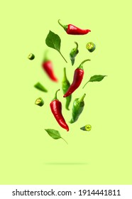Fliegende grüne und rote Chilischoten, Blätter einzeln auf grünem Hintergrund. Verzehrt für die Speisen, frische scharfe Pfeffer, würzige Gewürze zum Kochen, Kayenne-Pfeffer, Essen. Kreatives Konzept von Lebensmitteln, Gemüse
