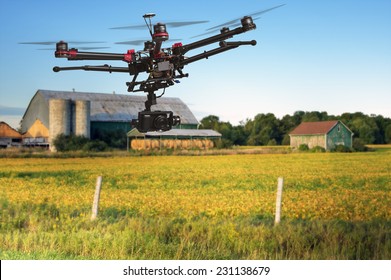 A flying helicopter with raised landing gears and a camera with blurred crop field and farm structures on a background highlighted by a sunset