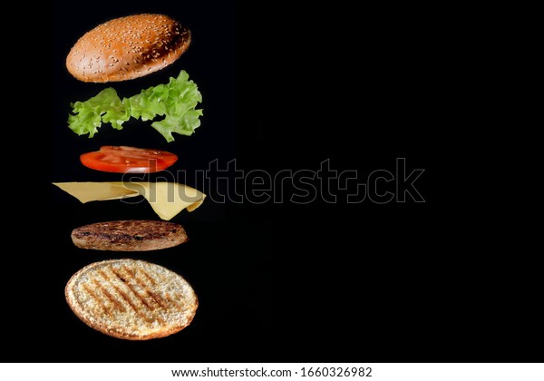 Flying ingredients burger or
cheeseburger on a small wooden cutting board isolated on a dark
background. Burger floating in the air above the table. Space for
text.
