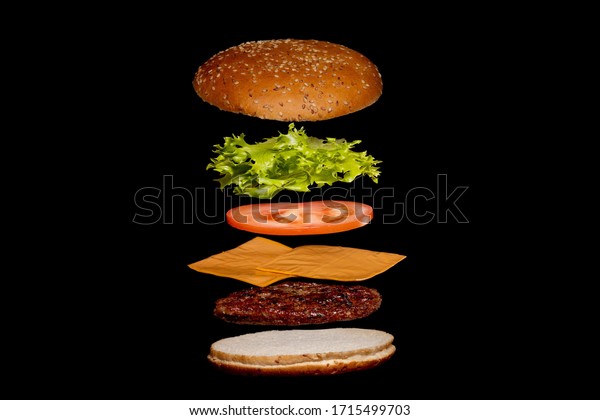 Flying ingredients burger or\
cheeseburger on a small wooden cutting board isolated on a dark\
background. Burger floating in the air above the table. Space for\
text.