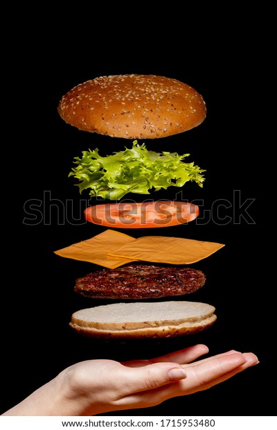 Flying ingredients burger or
cheeseburger on a small wooden cutting board isolated on a dark
background. Burger floating in the air above the table. Space for
text.
