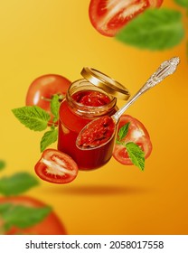 Flying Jar With Tomato Sauce. Jar Of Tomato Sauce, Ripe Slices Of Tomato And Spoon Fly In Air. Creative Food Background.