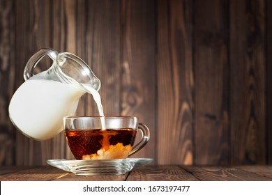 Flying Jug Pouring Milk Into Cup Of Tea On Wooden Table