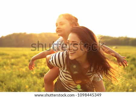 Flying kid girl laughing on the happy enjoying mother back on sunset bright summer background. Closeup portrait.