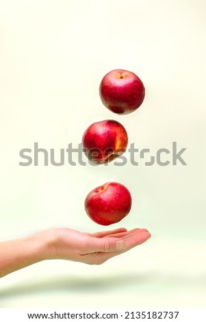 Flying levitating floating red ripe fresh juicy apples in air above female womens hand on green background. Levity summer fruits. Trendy, minimal Creative food.
