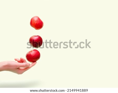 Flying levitating floating red ripe fresh juicy apples in air above female womens hand on green background. Levity summer fruits. Trendy, minimal Creative food.