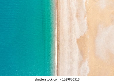 Flying over an empty sandy beach and beautiful emerald ocean waves. Top view landscape scene of waves rolling on an empty tropical beach