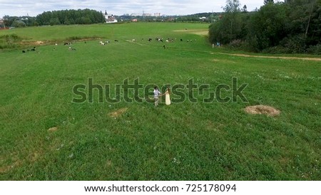 Flying over green field where the lovers walk. Aerial survey of margin where woman and man run. Field. Aerial survey of lovers run on the field