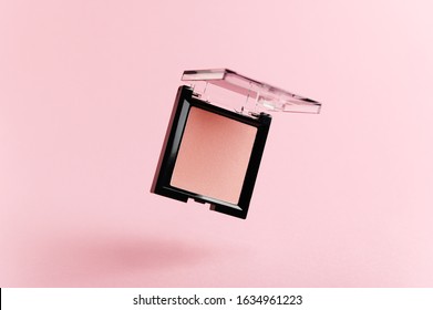 A flying packaging of pink blush on a pink background. Product of the beauty industry, female accessory of cosmetics levitate in the air. Base for makeup on the face, eyes and lips. Levitation.