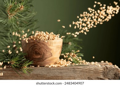 Flying peeled pine nuts on a dark green background. Nuts in a wooden bowl and cedar branch on a old wooden table. Copy space.