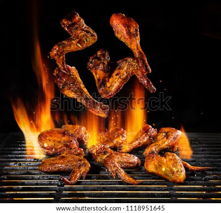 Flying pieces of chicken meat on grill with Fire flames. Isolated on black background. Barbecue and grilling. Very high resolution image