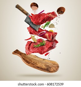 Flying pieces of raw beef steaks, with herbs, served on wooden
board. Meat chopper cutting the flesh. Concept of food preparation in low gravity mode. Separated on smooth gray background