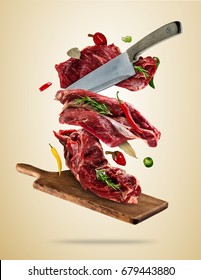 Flying Pieces Of Raw Steaks, With Ingredients For Cooking, Served On Woodenboard. Knife Cutting The Meat. Concept Of Food Preparation In Low Gravity Mode. High Resolution Image