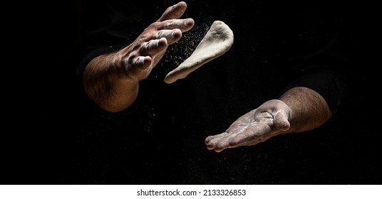 flying pizza dough with flour scattering in a freeze motion of a cloud of flour midair on black. Cook hands kneading dough. copy space.