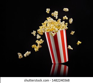 Flying popcorn from paper striped bucket isolated on black background, concept of watching TV or cinema.
