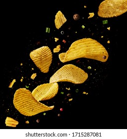 Flying potato chips with onions and peppers on a black background