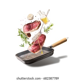 Flying Raw Beef Steaks, With Herbs, Oil And Spices With Grill Pan And Kitchen Utensils, Isolated On White Background, Front View. Flying  Food Concept