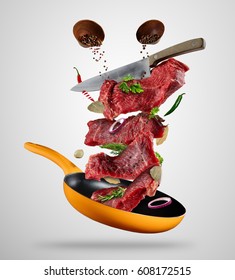 Flying Raw Steaks, With Ingredients For Cooking, From Pan. Knife Cutting The Meat. Concept Of Food Preparation In Low Gravity Mode. Separated On Gray Background