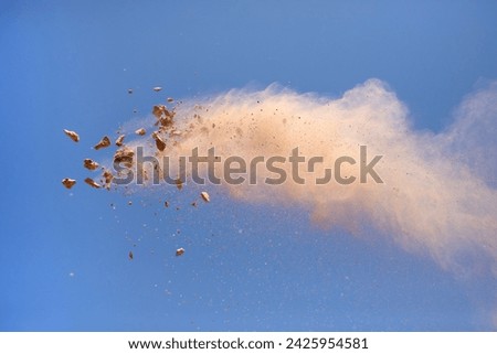 Flying rock debris and dust cloud against blue sky