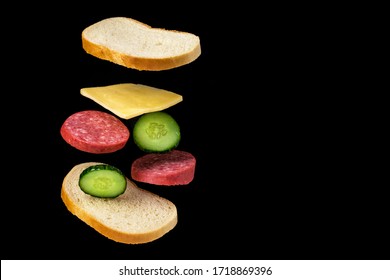 flying sandwich of bread, smoked sausage, cucumbers and cheese on a black background