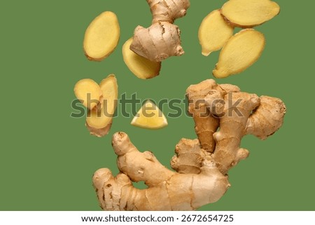Flying slices of fresh ginger root and lemon on green background