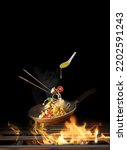 Flying Spaghetti with chicken and vegetables in a pan on fire - black background-Copy space