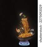 Flying Spaghetti with sea food and vegetables in a pan on fire - black background