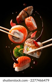 Flying sushi pieces are placed between chopsticks. Sushi and roll levitation with soy sause. Japanese food photo, black background