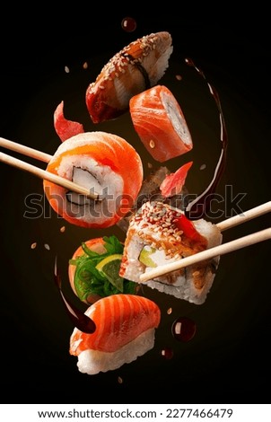 Flying sushi pieces are placed between chopsticks. Sushi and roll levitation with soy sause. Japanese food photo, black background vertical poster composition